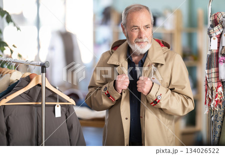 Elderly man chooses tries fashionable coat in clothing store 134026522