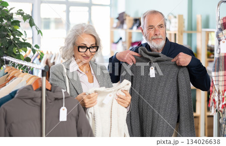 Elderly married couple chooses fashionable sweater in clothing store Elderly married couple chooses fashionable sweater in clothing store 134026638