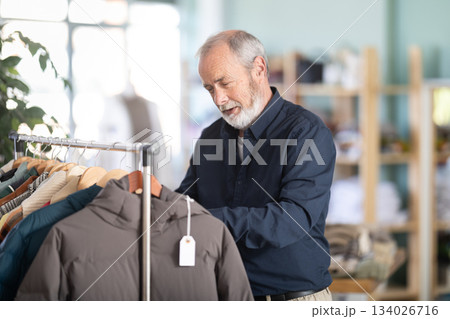 elderly man carefully chooses a down jacket in a store 134026716