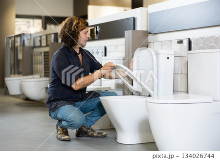 in plumbing department, male buyer checks for defects of toilet before purchasing toilet pan in plumbing department, male buyer checks for defects of toilet before purchasing toilet pan 134026744