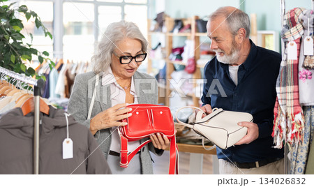 Mature couple spend time in shop and choose handbag Mature couple spend time in shop and choose handbag 134026832