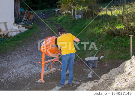 Woman puts water into the cement mixer 134027149