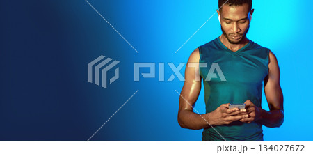 Fitness Application. Sporty Guy Using Smartphone Wearing Earphones Before Workout Standing On Blue Studio Background. Panorama Fitness Application. Sporty Guy Using Smartphone Wearing Earphones Before Workout Standing On Blue Studio Background. Panorama 134027672