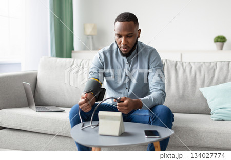 Hypertension. African Man Measuring Arterial Blood Pressure Having Health Problem Sitting On Sofa At Home. Hypotension And High Pressure Issue Concept. Selective Focus 134027774