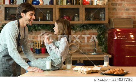 Millennial Father And His Little Daughter Having Fun In Kitchen, Baking Together, Laughing And Bonding While Preparing Homemade Pastry, Cute Girl Sitting On Table And Smiling, Copy Space Millennial Father And His Little Daughter Having Fun In Kitchen, Baking Together, Laughing And Bonding While Preparing Homemade Pastry, Cute Girl Sitting On Table And Smiling, Copy Space 134027780