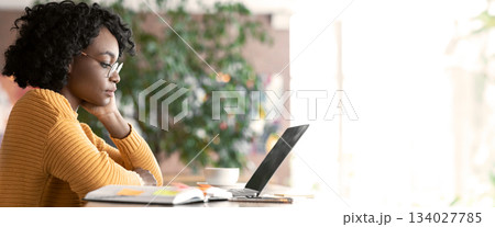 Pensive afro woman editor reading text on laptop, taking notes, working at cafe, copy space Pensive afro woman editor reading text on laptop, taking notes, working at cafe, copy space 134027785