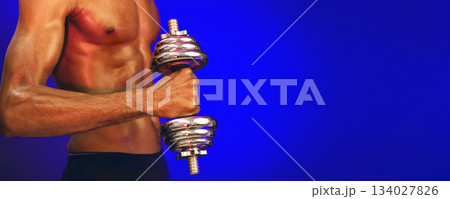 Bodybuilding Workout. Unrecognizable Strong Muscular Man Exercising With Dumbbells Over Blue Background In Studio, Focus On Dumbbell. Panorama Bodybuilding Workout. Unrecognizable Strong Muscular Man Exercising With Dumbbells Over Blue Background In Studio, Focus On Dumbbell. Panorama 134027826