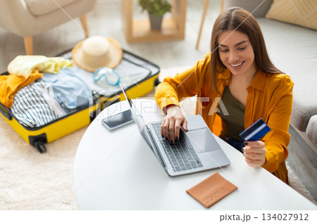 Happy young woman with credit card booking vacation at travel agency or making hotel reservation online, using laptop computer, planning abroad trip at home, copy space Happy young woman with credit card booking vacation at travel agency or making hotel reservation online, using laptop computer, planning abroad trip at home, copy space 134027912