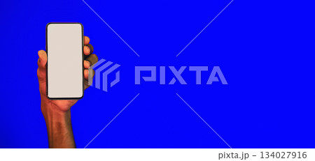 Mobile App. Male Hand Holding Smartphone With Blank Screen Advertising Application Over Blue Background. Mockup 134027916