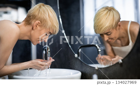 Cheerful Middle-Aged Lady Washing Face Standing In Bathroom. Hygiene And Skincare Routine. Selective Focus Cheerful Middle-Aged Lady Washing Face Standing In Bathroom. Hygiene And Skincare Routine. Selective Focus 134027969