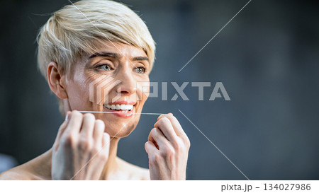 Toothcare Concept. Mature Lady Flossing White Teeth Standing Wrapped In Towel In Bathroom Indoor. Selective Focus, Copy Space 134027986