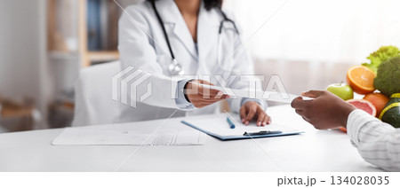 Dietologist giving prescription to client, clinic interior, cropped Dietologist giving prescription to client, clinic interior, cropped 134028035