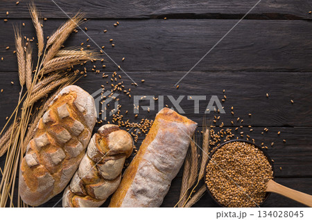 Bread border on wood with copy space background. Brown and white whole grain loaves still life composition with wheat ears scattered around. Bakery and grocery food store concept. 134028045