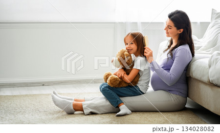Loving pregnant mother brushing her little daughter hair, sitting on floor at home, empty space Loving pregnant mother brushing her little daughter hair, sitting on floor at home, empty space 134028082