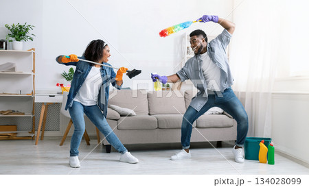 Cleaning Fun. Cheerful Black Couple Fooling While Tidying Up Their Flat, Playfully Fighting With Duster And Swab, Staying At Home, Free Space 134028099