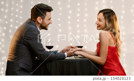 Elegant Couple Holding Hands In Restaurant, Having Romantic Dinner, Celebrating Anniversary Or Valentine's Day, Side View Elegant Couple Holding Hands In Restaurant, Having Romantic Dinner, Celebrating Anniversary Or Valentine's Day, Side View 134028123