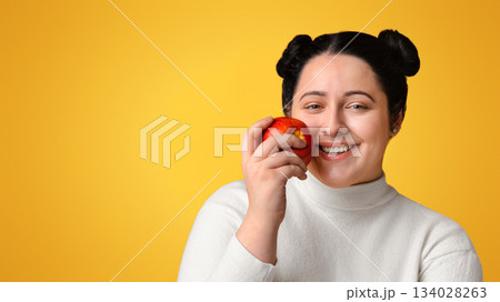 Organic Nutrition. Closeup Portrait Of Beautiful Happy Plump Girl Holding Red Apple And Sincerely Smiling, Posing Over Yellow Background, Empty Space Organic Nutrition. Closeup Portrait Of Beautiful Happy Plump Girl Holding Red Apple And Sincerely Smiling, Posing Over Yellow Background, Empty Space 134028263
