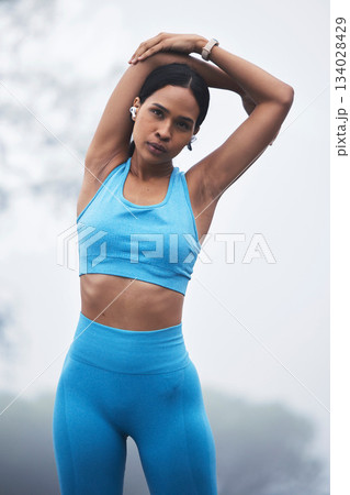 Arm stretching, woman portrait and runner exercise on a outdoor road in the mountains breathing. Workout, running training and fitness of a young female ready for sports and marathon run in mist 134028429