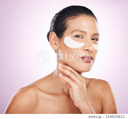 Face, skincare and woman with eye patches in studio isolated on a purple background. Portrait, dermatology and serious or mature female model with facial mask or collagen cosmetics for healthy skin. Face, skincare and woman with eye patches in studio isolated on a purple background. Portrait, dermatology and serious or mature female model with facial mask or collagen cosmetics for healthy skin. 134028812