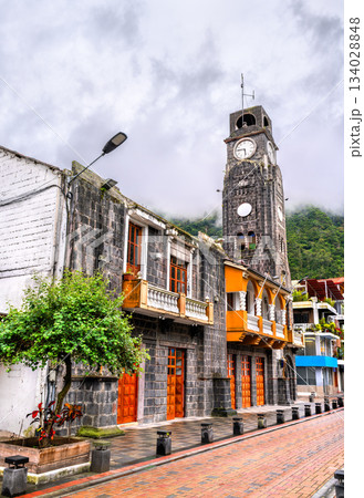 Municipal Palace or City Hall stands in Banos de Agua Santa, Ecuador. Historic stone building features tall clock tower and orange balconies near the central park 134028848