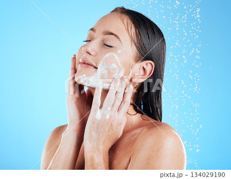 Shower, facial and woman washing face with soap on blue background for grooming, cleaning and wellness. Skincare, bathroom and happy girl with foam product for hygiene, hydration and beauty in studio 134029190