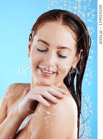 Water, soap and woman washing or shower in studio for skincare, wellness and clean body or self care. Happy female aesthetic model splash for cleaning, hygiene and skin cosmetics on blue background 134029200