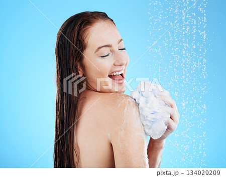 Woman in shower, laughing and happy with soap, hygiene and water drops with skincare on blue background. Washing, grooming and cosmetic care, female cleaning body with foam and mockup in studio 134029209