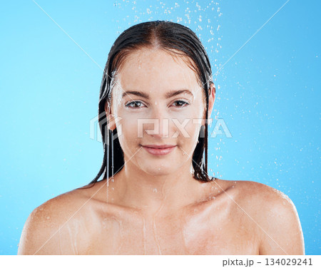 Shower portrait, water and woman in a studio with a smile from cleaning and skincare. Wellness, bathroom and beauty routine of a female model relax from dermatology and self care with blue background 134029241