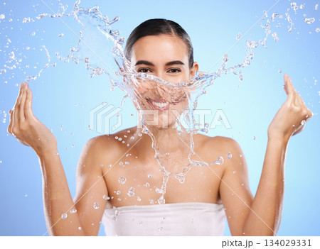 Water splash, portrait or happy woman and face wash for skincare or hygiene on blue background in studio. Smile, wet or model and clean hands in wellness washing, beauty grooming or facial treatment Water splash, portrait or happy woman and face wash for skincare or hygiene on blue background in studio. Smile, wet or model and clean hands in wellness washing, beauty grooming or facial treatment 134029331