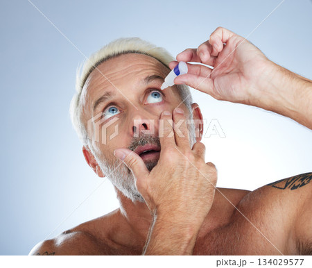 Eye drops, senior man and studio with medical, healthcare and wellness pharmaceuticals. Isolated, blue background and male model with dry eyes and medicine for vision solution and allergy product Eye drops, senior man and studio with medical, healthcare and wellness pharmaceuticals. Isolated, blue background and male model with dry eyes and medicine for vision solution and allergy product 134029577