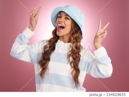 Fashion, happy and portrait of woman with peace sign on studio background for confidence, excited and emoji. Beauty, facial expression and girl smile with trendy style, funky cosmetics and laughing 134029635