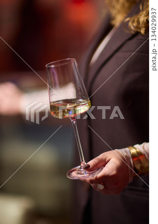 Refined woman savoring amber glass drink, Closeup of woman enjoying sophisticated wine experience, Fashionable lady gracefully holding glass of golden wine at classy Refined woman savoring amber glass drink, Closeup of woman enjoying sophisticated wine experience, Fashionable lady gracefully holding glass of golden wine at classy 134029937