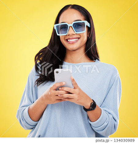Phone, smile and portrait of woman with sunglasses in yellow studio for social media, website and internet. Communication, mockup space and happy girl on smartphone for chat, message and network 134030989