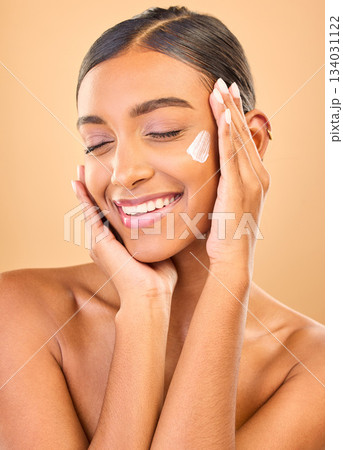 Face, skincare smile and woman with cream in studio isolated on a brown background. Dermatology cosmetics, eyes closed and happy Indian female model with lotion, creme or moisturizer for skin health. 134031122