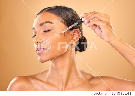 Face, skincare serum and woman with eyes closed in studio isolated on brown background. Dermatology, cosmetics and Indian female model with hyaluronic acid, retinol or essential oil for healthy skin. 134031141
