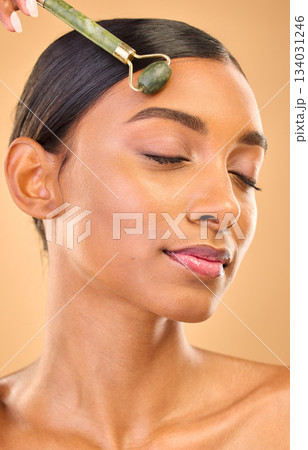 Face, skincare roller and woman with eyes closed in studio isolated on a brown background. Dermatology, facial massage and Indian female model with jade crystal for healthy skin treatment and beauty. Face, skincare roller and woman with eyes closed in studio isolated on a brown background. Dermatology, facial massage and Indian female model with jade crystal for healthy skin treatment and beauty. 134031246