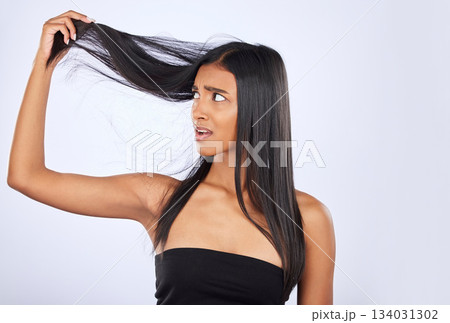 Hair damage, breakage and shock of a frustrated woman isolated on a white background in studio. Bad, unhappy and an Indian girl sad about split ends, holding tangled hairstyle and frizzy haircare 134031302