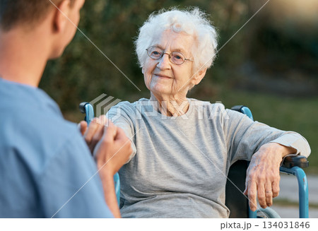 Senior woman, wheelchair and caregiver holding hands with patient for empathy, support and care outdoor for communication and air. Man nurse and old woman talking rehabilitation at nursing home 134031846