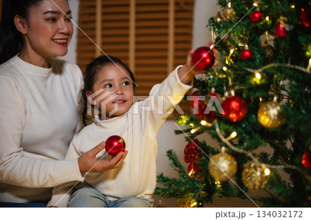 mother and toddler girl decorating Christmas tree in home at night mother and toddler girl decorating Christmas tree in home at night 134032172