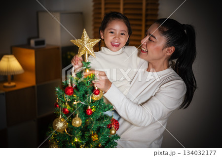 mother and toddler girl decorating star on Christmas tree in home at night mother and toddler girl decorating star on Christmas tree in home at night 134032177