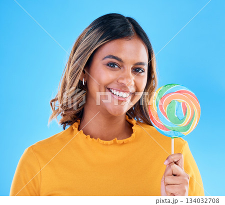 Portrait, lollipop and a woman on a blue background in studio wearing heart glasses for fashion. Smile, candy and sweet with an attractive young female eating a giant snack while feeling happy Portrait, lollipop and a woman on a blue background in studio wearing heart glasses for fashion. Smile, candy and sweet with an attractive young female eating a giant snack while feeling happy 134032708