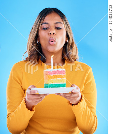 Birthday cake, woman and blow candles in studio, blue background and celebration. Female model, dessert and wishing at party, flame and special event, rainbow treat or celebrate happiness on backdrop 134032712
