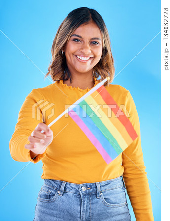 Portrait, flag and gay pride with a woman on a blue background in studio feeling proud of her lgbt status. Smile, freedom and equality with a happy young female holding a symbol of inclusion Portrait, flag and gay pride with a woman on a blue background in studio feeling proud of her lgbt status. Smile, freedom and equality with a happy young female holding a symbol of inclusion 134032728