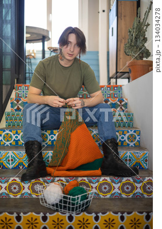 Feminine hipster man crochet handmade use hook knitting needles and wool yarn relaxing on couch Feminine hipster man crochet handmade use hook knitting needles and wool yarn relaxing on couch 134034278
