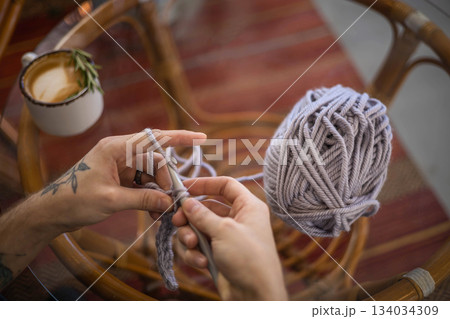 Male hands crochet handmade artwork use wool yarn and hook over table with coffee top view 134034309