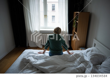 Middle aged woman sits on bed in morning, tired unmotivated, dealing with depression and burn out. 134034584
