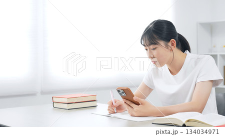 スマホを見ながら勉強する10代女性 134034971