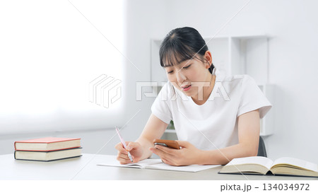 スマホを見ながら勉強する10代女性 スマホを見ながら勉強する10代女性 134034972
