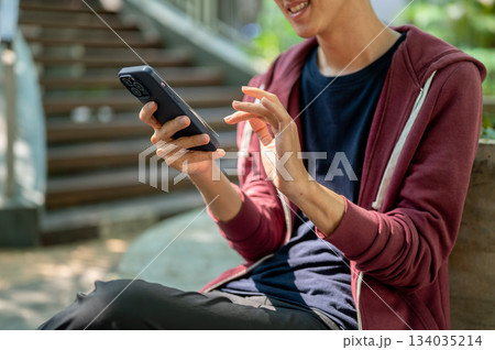 Close up of smiling man looking at his phone watching video or making a call sitting near the stair Close up of smiling man looking at his phone watching video or making a call sitting near the stair 134035214