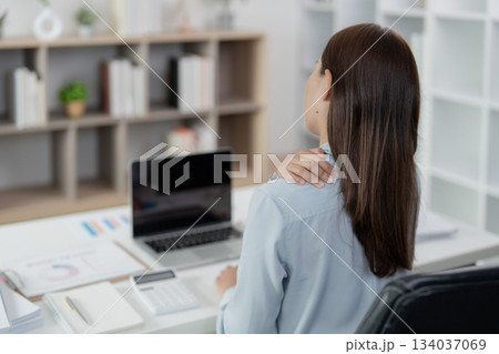 Office Syndrome: Woman massaging her shoulder while seated at her desk 134037069